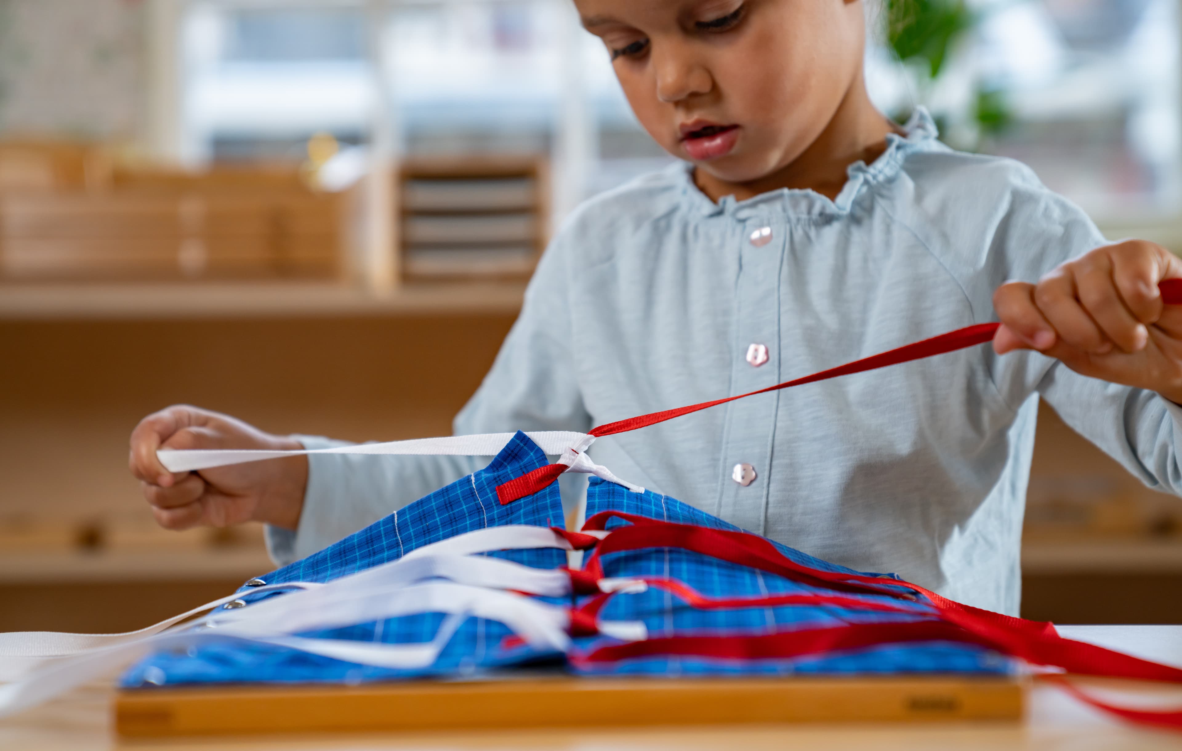Ein Mädchen bindet mit einem Nienhuis Kleinkind-Anziehrahmen an einem Tisch und zieht die Schleifen aus dem Rahmen.