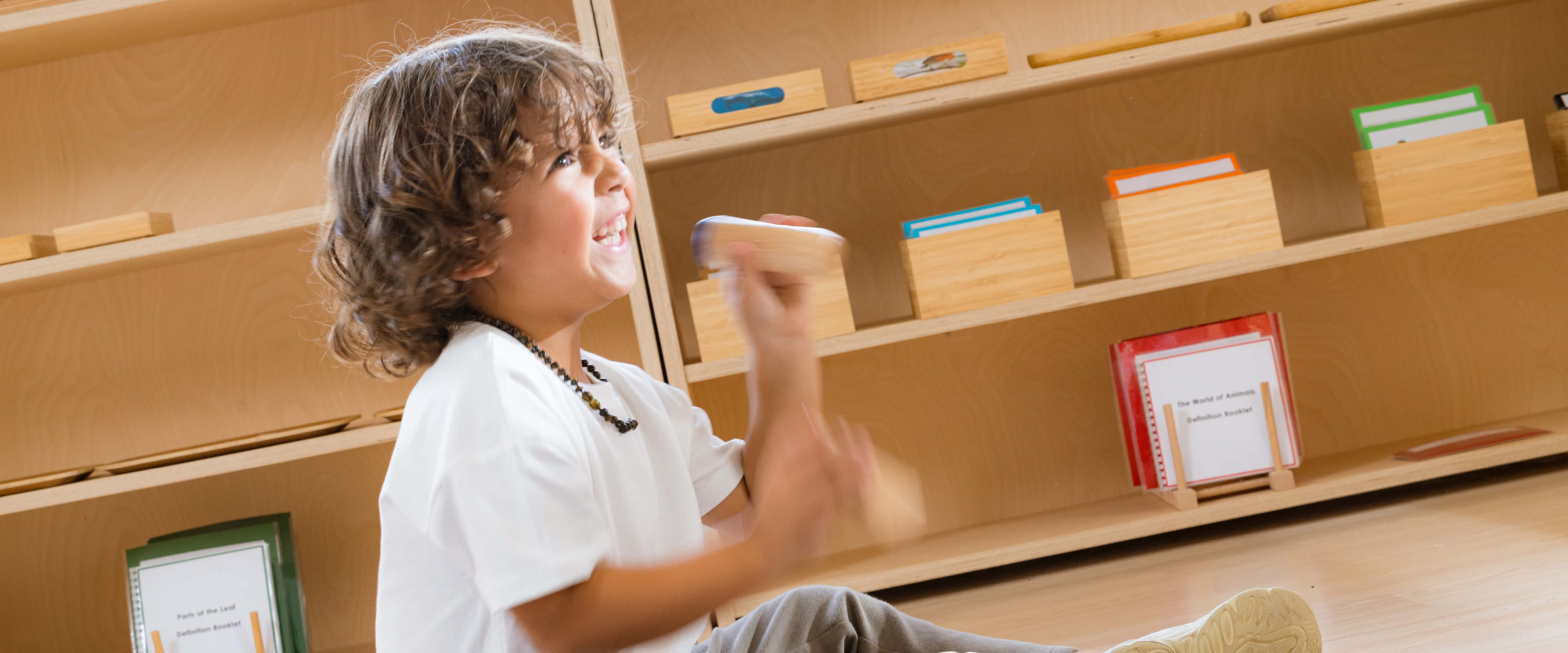 Boy with a big smile working on a floor mat with the Montessori Sound Boxes.