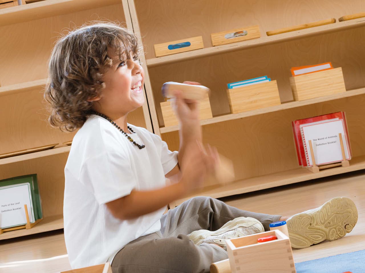 Boy with a big smile working on a floor mat with the Montessori Sound Boxes.