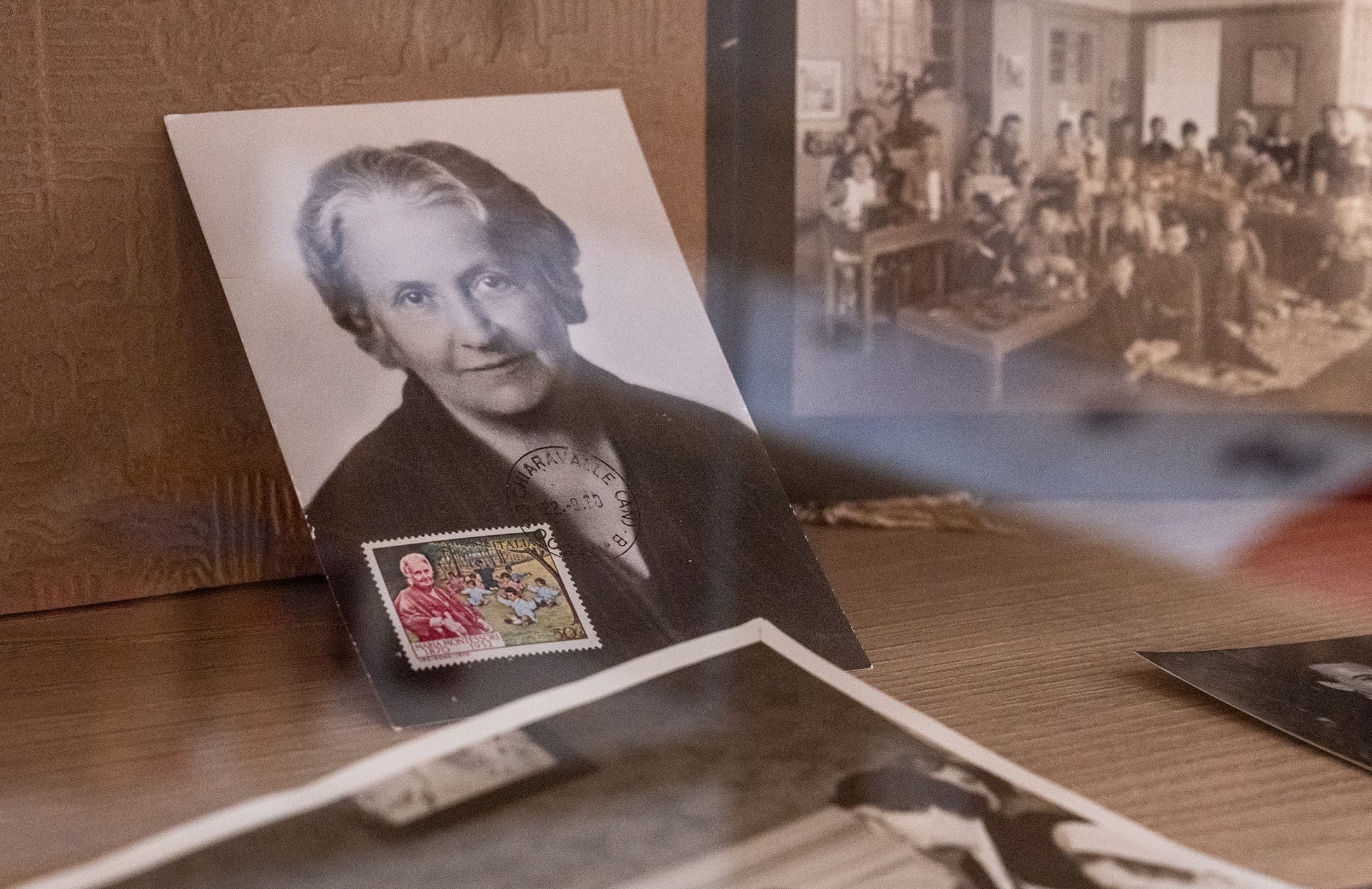 Ein altes Foto von Maria Montessori mit dazugehörigen Briefmarken und alten Klassenfotos im Hintergrund.