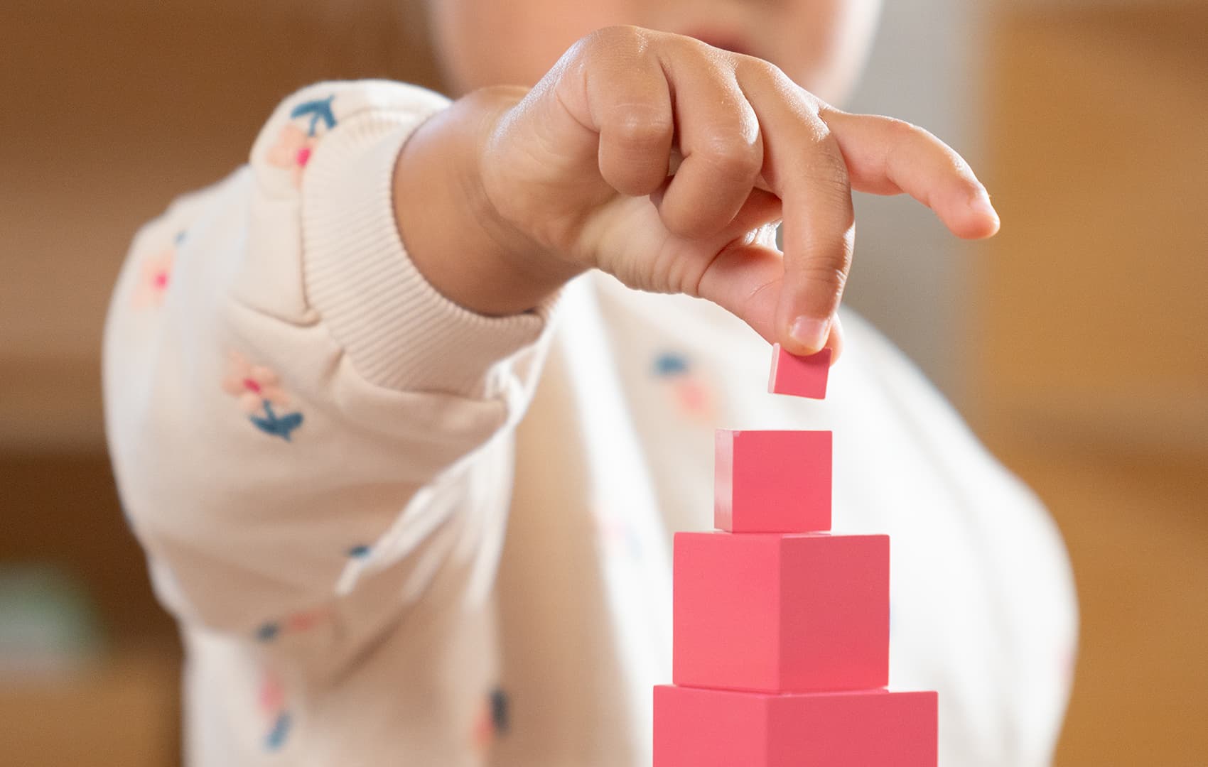 A child's hand stacking pink blocks from a Pink Tower.