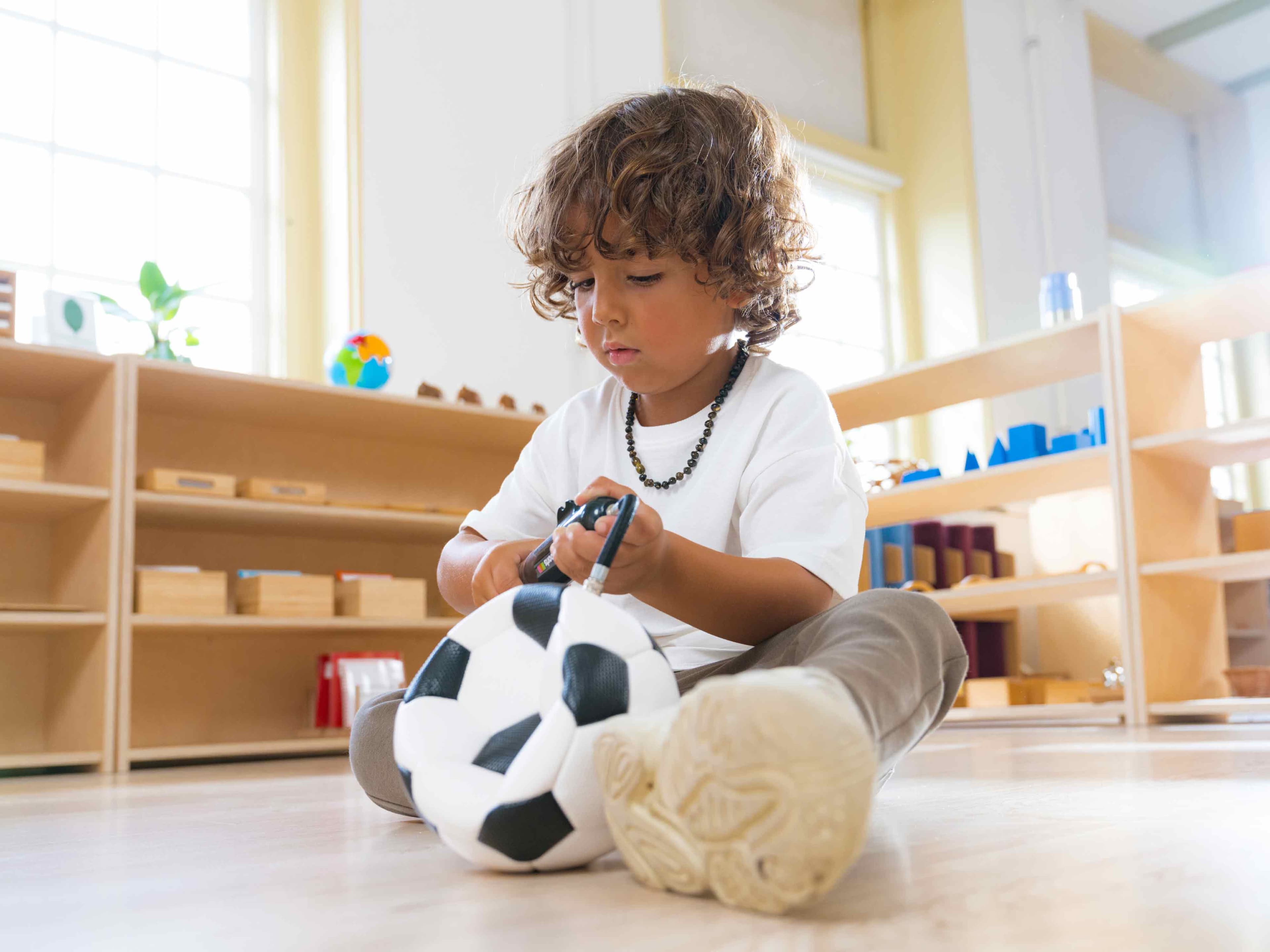 A boy sitting on the floor inflating a Montessori football.