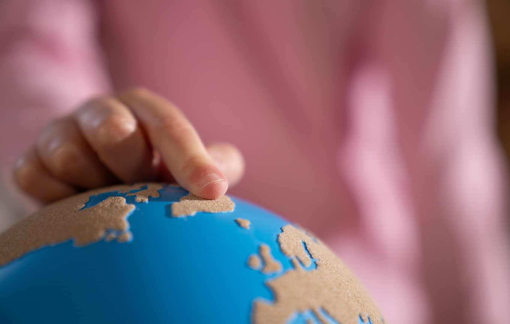 A close-up of a child's finger touching a rough-smooth globe from Nienhuis.