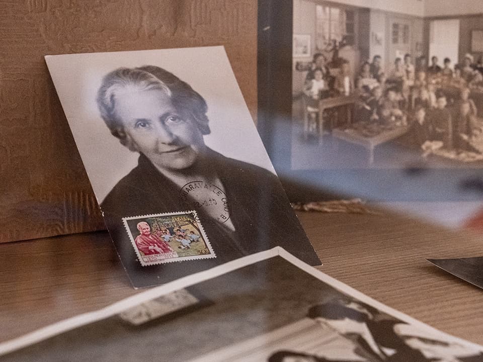 An old photo of Maria Montessori with accompanying stamps and old class photos in the background.