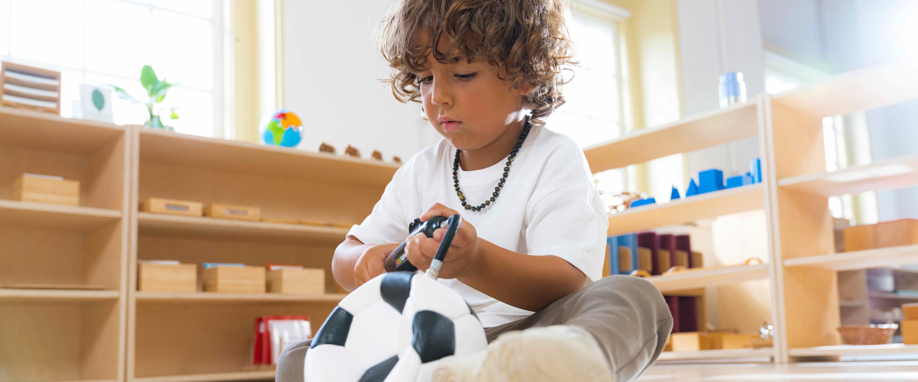 A boy sitting on the floor inflating a Montessori football.