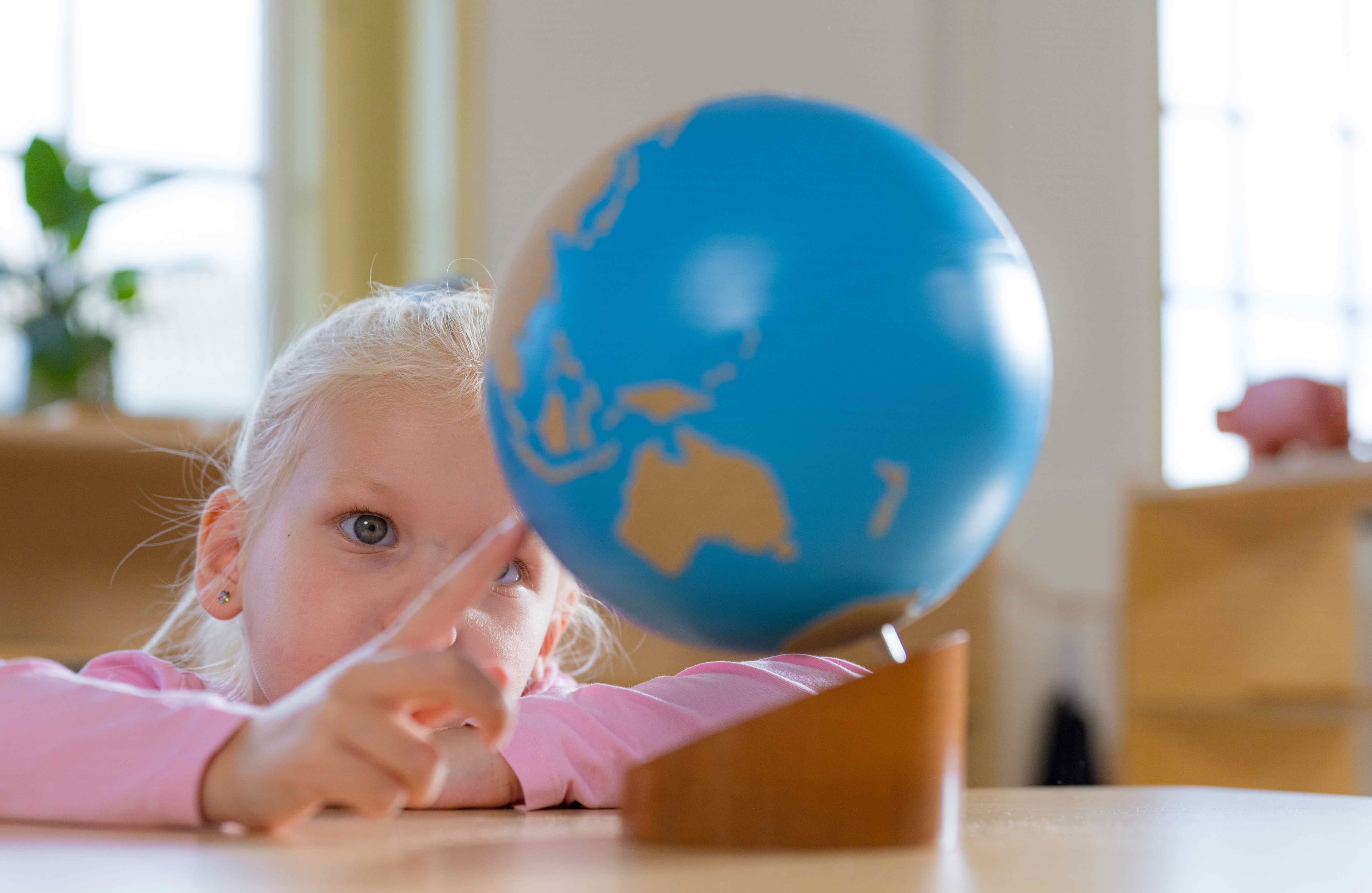 Ein Mädchen zeigt mit ihrem Zeigefinger auf einen Montessori rauen-glatten Globus, der auf einem Tisch steht.